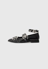 Black pointed flat shoe with three silver buckled straps, ankle strap with eyelets, and metallic detail on toe area.