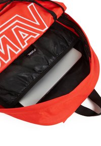 Zaino rosso brillante con un grande logo bianco, interno nero e scomparto imbottito per un laptop. Presenta spallacci e zip neri.