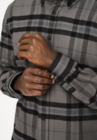 Camicia in flanella a quadri grigi e neri con tessuto testurizzato, design con bottoni e maniche lunghe. Presenta linee blu a contrasto e bottoni neri.