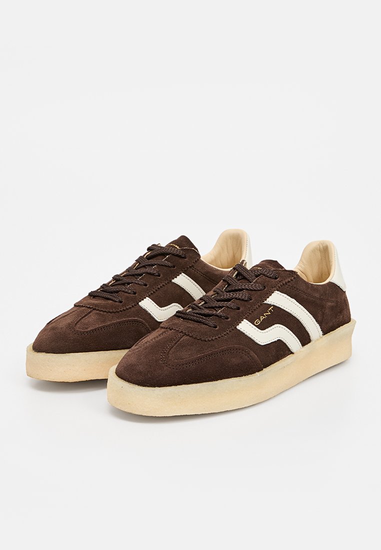 Baskets en daim marron avec une semelle de couleur crème, dotées de bandes latérales blanches, d'un bout rond et d'un design à lacets. Accent de logo doré sur le côté.