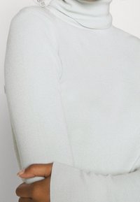 Pull à col roulé gris clair en texture côtelée. Manches longues avec des poignets ajustés. Matériau doux soulignant le confort et la chaleur.