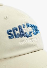 Beige pet met blauwe geborduurde tekst "SCALPERS" en kleinere witte tekst eronder met de tekst "WE KOMEN NAAR DE VK".