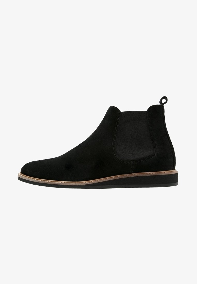 Bottine Chelsea en daim noir avec panneau latéral élastique, garniture marron le long de la semelle, languette à l'arrière et petit talon empilé.