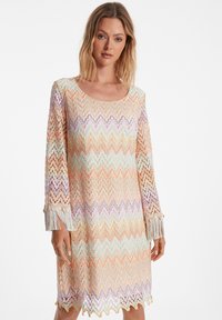 Robe longueur genou au motif en zigzag avec des couleurs pastel — pêche, lavande, menthe — dotée de manches à franges et d'un col rond.