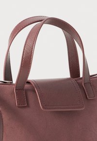 Close-up of a mauve handbag showing textured double handles and a matching flap on suede material against a plain background.