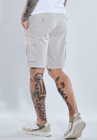 Light gray cargo shorts featuring side pockets, a smooth texture, and a relaxed fit, paired with white and beige sporty sneakers.