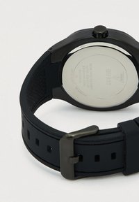 Musta silikoninen rannekello ruostumattomalla teräksellä takana, vesitiivis jopa 50 metriin asti, metallinen solkikiinnike.