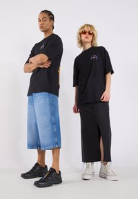 Black graphic t-shirts, blue denim shorts, and a black denim skirt, paired with black and white sneakers, featuring slit and fringe details.