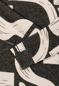 Tela gris con un patrón audaz, abstracto en crema y negro. El material es suave con un acabado texturizado. El diseño incluye formas superpuestas.