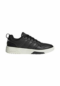 Baskets basses noires Adidas avec semelle blanche, lacets à l’avant et les trois bandes caractéristiques sur le côté.