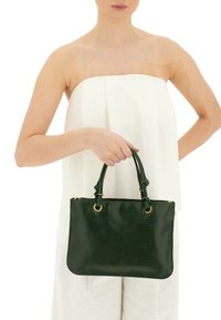 Borsa a mano verde in pelle con una texture liscia, forma rettangolare, manici annodati e dettagli in metallo dorato. Il design è minimalista e raffinato.