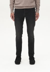 Schwarze Jeans mit einer slim fit Passform und leichter Verwaschung, kombiniert mit einem beigen Strickpullover. Die Schuhe sind aus schwarzem Wildleder.