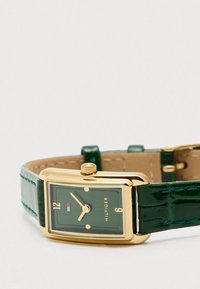 Green rectangular watch with gold-tone case, contrasting green dial, white hour markers, and a glossy green crocodile leather strap.