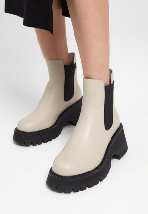 Beige Leder-Ankle-Boots mit schwarzen elastischen Seitenteilen, dicker schwarzer Sohle und strukturierten Kanten. Glatte Oberfläche und rundes Zehen design.