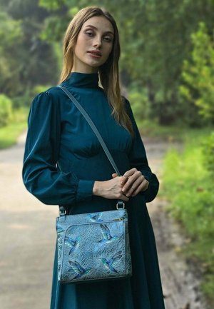 Blauwe en groene handtas met geborduurde bloemen- en kolibripatronen, vergezeld van een verstelbare grijze schouderband en een ritssluiting.