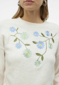 Pull crème avec broderie florale bleue et verte, accompagné d'accents jaunes. Texture douce et design à col rond.