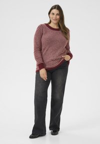 Czerwono-różowy sweter w paski, dziany, z okrągłym dekoltem i ściągaczami, w połączeniu z ciemnymi dzwonami i czarnymi butami.
