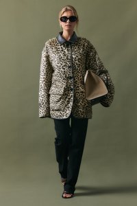 Cappotto in stampa leopardata con colletto in pelle nera, bottoni frontali e due tasche, abbinato a pantaloni neri e una borsa beige. Tessuto texturizzato.