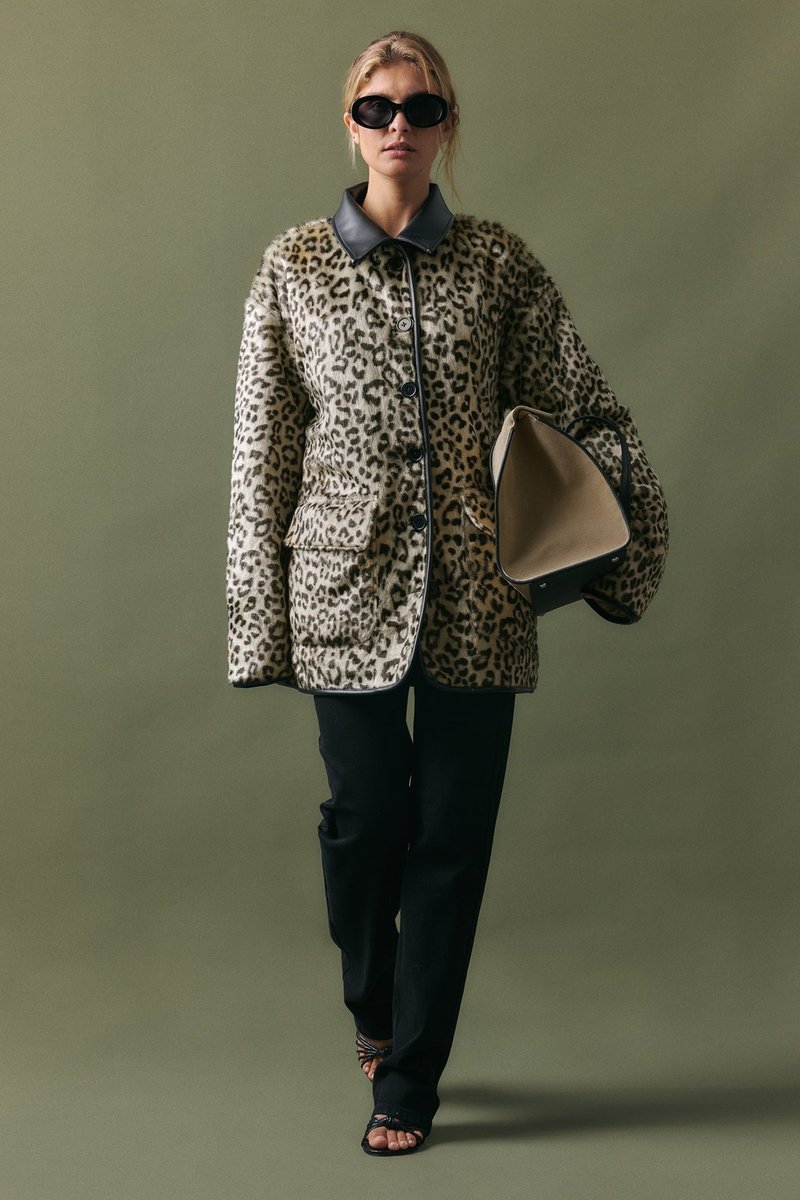 Cappotto in stampa leopardata con colletto in pelle nera, bottoni frontali e due tasche, abbinato a pantaloni neri e una borsa beige. Tessuto texturizzato.