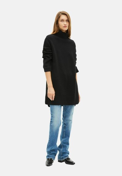 Schwarzer übergroßer Pullover mit hohem Kragen und gerippten Bündchen, kombiniert mit hellblauen Schlagjeans und schwarzen Schuhen. Glatte Textur und lässige Passform.