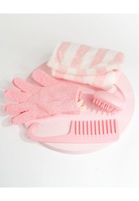 Rosa hårvårdsset med exfolierande handskar, bredtandad kam, hårbottenmassager och randig handduk på en rund rosa yta.