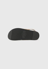 Suela de zapato de goma negra, texturizada con surcos horizontales. Logo del fabricante embossado en el centro, diseño circundante de tono claro.