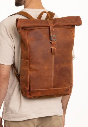 Mochila de cuero marrón tipo roll-top con correas ajustables, cierre de hebilla metálica y detalles de costura visibles. Bolsillo trasero en el lateral.