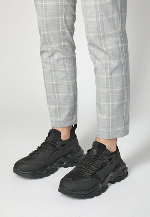 Black athletic sneakers featuring a textured mesh upper, sleek design, and a thick rubber sole with prominent tread pattern.