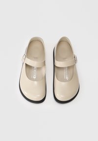 Scarpe beige stile Mary Jane con una finitura liscia e lucida, punta rotonda e una cinghia con una fibbia in metallo. Suola in gomma nera.