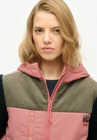 Roze en olijfgroene ritsjack met capuchon, voorzien van een textuur, ribbenpanelen en een geborduurd embleem op de borst.