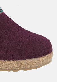 Zoccoli in feltro di lana bordeaux con finitura testurizzata e suola in sughero beige; presentano una leggera curvatura alla punta per comfort e stile.