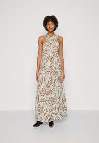 Abito maxi in tessuto azzurro chiaro con stampa floreale marrone. Presenta un collo incrociato, vita aderente e gonna fluida. Stivali neri alla caviglia.