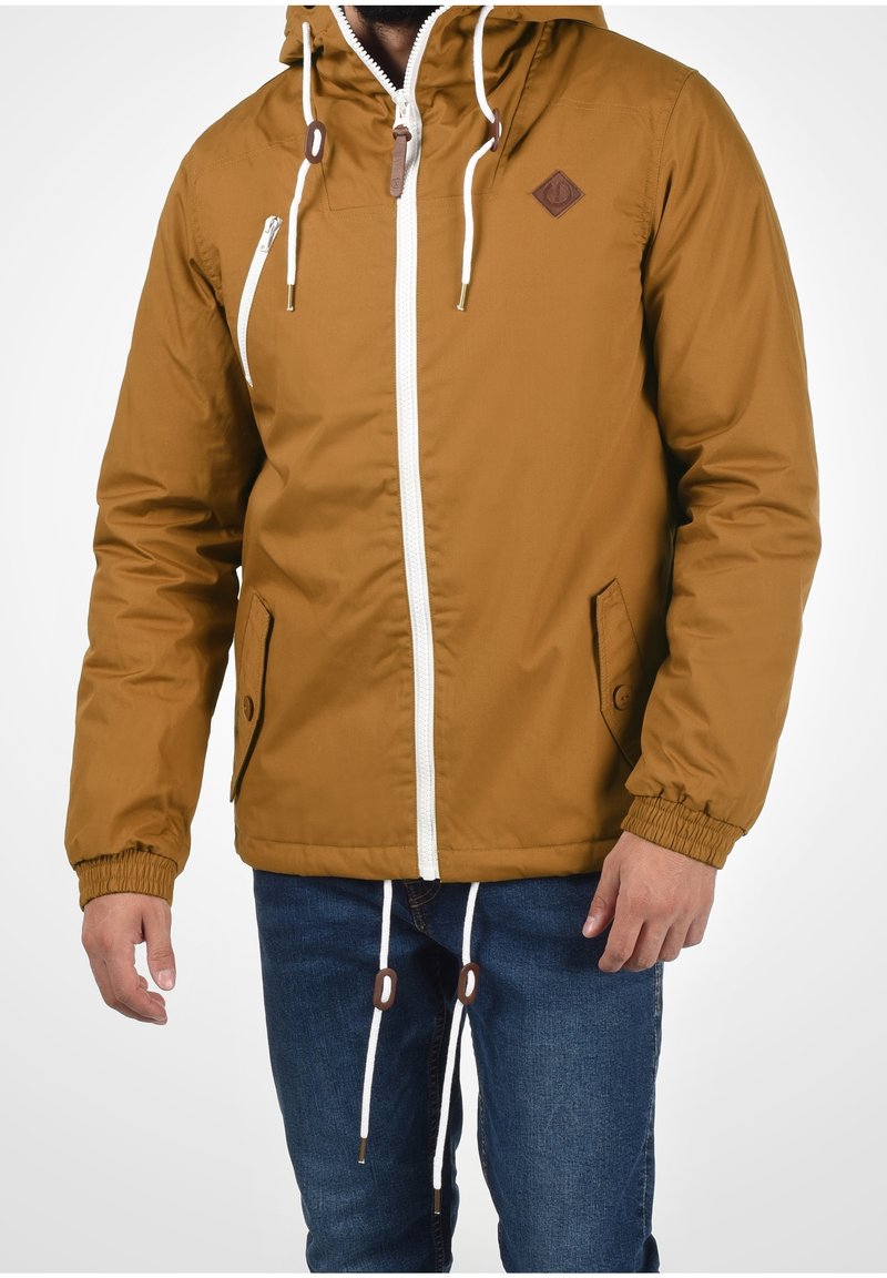 Brun hættejakke med hvid lynlås, elastiske manchetter og to forlommer. Har et diamantlogo-patch og kontrasterende snore.