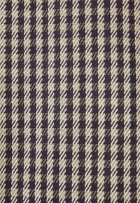 Tissu tissé avec un motif pied-de-poule en bandes alternées de gris foncé et de beige, présentant une surface texturée.