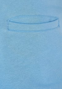 Ljust blått tyg med en slät textur har en liten, horisontell sydd ficka. Designen är enkel och minimalistisk.