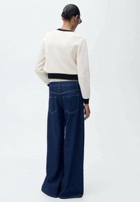 Pull blanc court avec bord noir, associé à un jean en denim bleu foncé à jambes larges avec poches arrière et une texture lisse.
