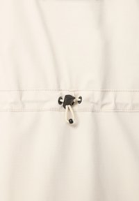 Beige stof med en glat tekstur. Har en sort toggle og snor til justering, sikret med en subtil sømdetalje.