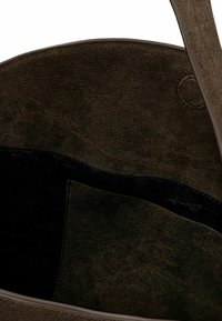 Torba na ramię z ciemnobrązowego zamszu o miękkiej fakturze, wyposażona w czarne wnętrze oraz kieszeń po bokach. Prosty design z pojedynczym paskiem na ramię.