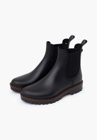 Bottines Chelsea en caoutchouc noir avec des panneaux élastiques sur les côtés, des coutures orange contrastantes, des semelles texturées et des languettes à l'arrière.