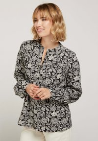 Blouse florale noir et blanc avec un col, des manches longues et une fermeture à boutons, présentant des motifs botaniques complexes et une coupe décontractée.