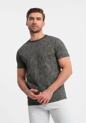 T-shirt verde scuro con motivo a foglie, maniche corte e colletto tondo. Il tessuto appare morbido con un dettaglio di stampa testurizzata.