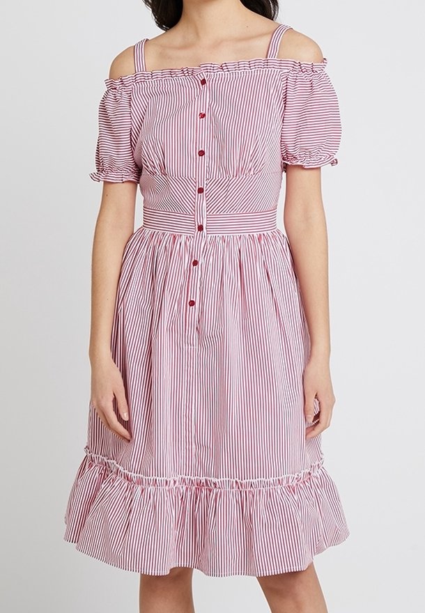 Femme portant une robe rayée verticale rouge et blanche, épaules dénudées, manches bouffantes, boutons sur le devant, taille cintrée et ourlet volanté.