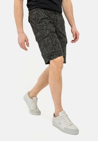 Zwarte cargoshorts met een bladerenpatroon, voorzien van meerdere zakken en een relaxte pasvorm. Draagt met witte sneakers voor een casual look.