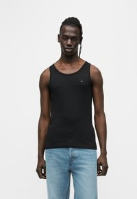 Μαύρο βαμβακερό αμάνικο μπλουζάκι με στρογγυλή λαιμόκοψη και φαρδιές μασχάλες. Διαθέτει ένα μικρό λογότυπο στο στήθος. Φοριέται με ανοιχτόχρωμα τζιν.