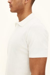 Valkoinen lyhythihainen poolopaita, jossa on ribbineulottu kaulus ja hihansuut. Valmistettu pehmeästä materiaalista, jossa on napillinen nappilista ja sileä pinta.