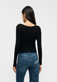 Μαύρο ριμπ πλεκτό με φαρδιά λαιμόκοψη και μακριά μανίκια, συνδυασμένο με μπλε τζιν παντελόνι που διαθέτει ραφές στις πίσω τσέπες και ελαφρώς ξεθωριασμένο φινίρισμα.