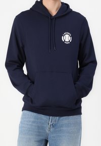 Námořnická mikina vyrobená z bavlněné směsi, má klokaní kapsu a nastavitelné stahovací šňůrky, s bílým logem Lacoste Paris na hrudi.