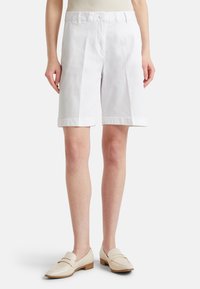 Pantaloni corti bianchi in cotone con taglio dritto, dotati di chiusura anteriore con bottone e orli arrotolati, abbinati a mocassini di colore chiaro.