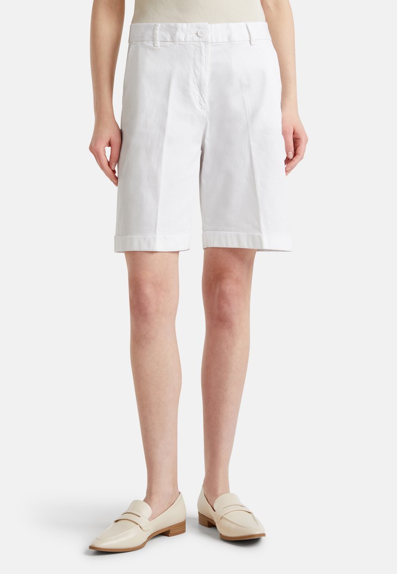 Pantaloni corti bianchi in cotone con taglio dritto, dotati di chiusura anteriore con bottone e orli arrotolati, abbinati a mocassini di colore chiaro.