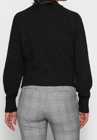 Svart stickad tröja med hög halsringning, ribbat avslut och långa ärmar. Tillsammans med grå rutiga byxor med skräddarsydd passform.